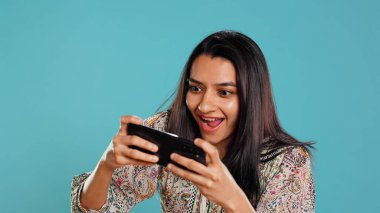 Happy woman playing videogames on smartphone, celebrating after defeating foes, doing clenching hand gesture. Player swiping phone screen, thrilled about winning game, studio background, camera B clipart