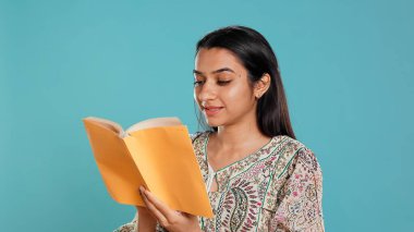 Gülümseyen neşeli bir kadın, kitap okurken eğleniyor, stüdyo arka planında izole bir şekilde kitap tutuyor. Neşeli insan, eğlendirici romanlardan, boş zamanlardan ve B kamerasından memnun.