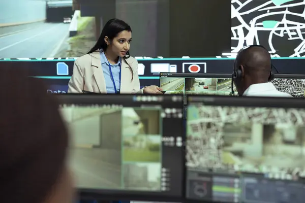 stock image Indian supervisor gives instructions to her team in monitoring room, working on giving insight to truck drivers couriers about the best routes to avoid traffic. GPS tracking on satellite map.