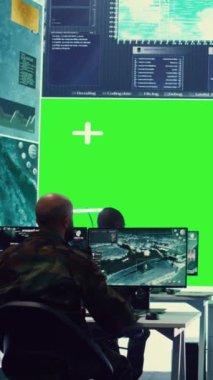 Büyük bir ekranda çalışan dikey video çeşitliliği grubu, komuta merkezindeki askeri operasyonlara yardım etmek için yeşil ekrana bakıyor ve istihbarat topluyor. Ordu tesisi