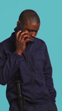 İşteki güvenlik görevlisinin dikey video görüntüsü. Mülkü denetlerken arkadaşlarıyla konuşmak için telefon kullanıyor. Özel güvenlik görevlisi arkadaşlarıyla telefon görüşmesi yapıyor, stüdyo arkaplanı, kamera B