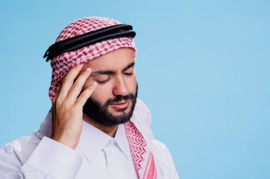 Yorgun düşmüş, gözleri kapalı bir müslüman migrenden muzdaripken tapınağı tutuyor. Geleneksel giysiler giyen bir Arap yüksek tansiyonu varken acı hisseder ve kafaya dokunur.