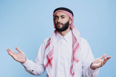 Geleneksel giyinmiş kafası karışmış Müslüman adam ellerini açıyor ve belirsizlik portresi çiziyor. Kafası karışmış bir Arap omuz silkiyor, kollarını açıp kameraya bakıyor.