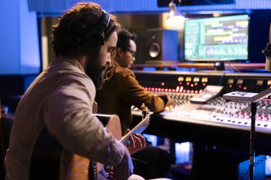 Şarkı sözü yazarı kontrol odasında gitarıyla yeni bir şarkı yaratıyor, elektro akustik enstrüman çalıyor ve müzik yapımcısının yanında şarkı söylüyor. Genç sanatçı canlı performans sergiliyor, karıştırma konsolunda müzik düzenliyor.