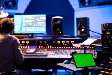 Profesyonel stüdyodaki kontrol odasında model ekranı olan bir cihaz, panel düğmeleri ya da kaydırma çubuklarıyla müzik üreten ve kaydeden bir ses teknisyeni. Yapımcı stereo teçhizatla parçaları düzenliyor.
