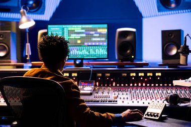Müzik yapımcısı, kontrol odasında ses konsolu ve bilgisayardaki profesyonel yazılımla sesleri düzenliyor ve işliyor. Üretim mühendisi motorlu faders ve çevirme düğmeleri kullanıyor.