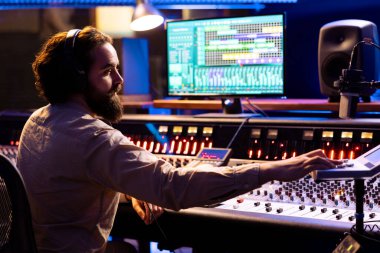 Profesyonel stüdyoda çalışan ses mühendisi parçaları karıştırıp, ana hatları yapmak için kontrol odasında uzman kurgu müziği yapıyor. Ses teknisyeni torpido gözünde faders ve düğme kullanıyor, teknik ekipman.