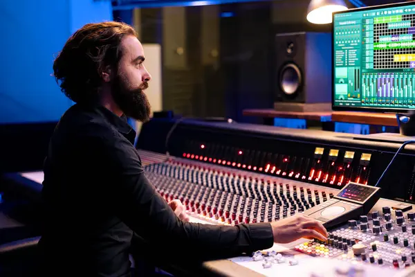 stock image Tracking engineer editing new music with digital audio software and mixing console in control room, working in post production at studio. Audio technician operates sliders and knobs.