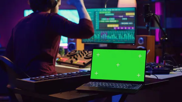 stock image Music engineer editing audio recordings on mixing console and daw software, having a laptop with greenscreen in home studio. Artist producing a new song with acoustical engineering tools. Camera A.