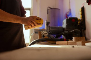 Kereste bloklarını zımparalamak için elle zımpara kağıdı kullanan bir adam, marangozhanede mobilya montajı yapıyor. Marangoz ahşabı düzleştiriyor, cilalamadan önce görünüşünü düzeltiyor.