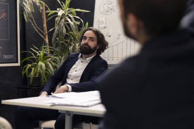 Bilgi grafiklerini değerlendirmek ve nelerin geliştirilebileceğini anlamak için veri raporlarıyla sunulan bir sunumu dinleyen iş analisti, problem çözme konferansı. Uzman tanımlama sorunları.