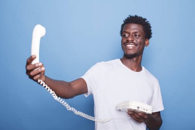 Gülümseyen Afrikalı Amerikalı beyefendi sabit telefon kablosuna bakıyor. Konuşmadan önce, afro saçlı siyahi bir adam ayakta ve telefonu kavrıyor..