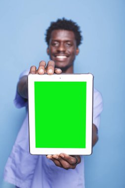 Mavi önlük giyerken yeşil ekranı gösteren tabletle ayakta duran erkek doktorların yakın çekimi. Siyah adam elinde boş telif alanı kromatuar şablonu ile kameraya doğru dijital aygıt tutuyor.