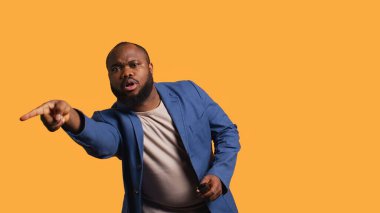 Televizyonda spor maçı izleyen bir adam, çenesini düşüren bir olaya kapılmış, ekrana dikkatle bakıyor. Vahşi futbol yarışması yayınından büyülenmiş bir adam, stüdyo arka planı, kamera B