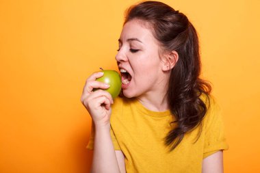 Sağlıklı görünümlü bir kadın yeşil bir elmayı ısırırken kamerada görülüyor. Kafkasyalı vejetaryen, doğal beslenme ve taze yiyecek kaynağı olarak organik tatlı abur cuburları teşvik ediyor. Yetişkinler meyve yiyor..