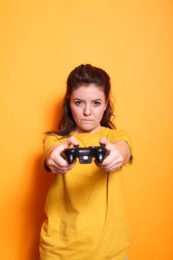 Odaklanmış bir kadın kameranın önünde kablosuz bir kumanda tutuyor. Genç yetişkin bir kadın, stüdyodaki bir konsolda elinde joystick ile oyun oynuyordu..