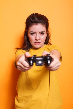 Kameranın önünde elinde kablosuz kontrol cihazı olan odaklanmış bir kadının portresi. Stüdyoda, genç bir kadın yetişkin oyun konsolunda oynamak için joystick kullanıyor..