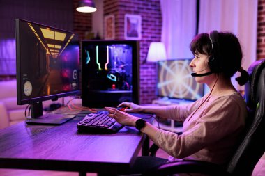 Profesyonel oyuncu yoğun online çok oyunculu video oyununda canlı oturma odasından neon ışıklarla canlı yayında yarışıyor. Deneyim kazanmak için oyun bilgisayarı ve kulaklık kullanan bir kadın