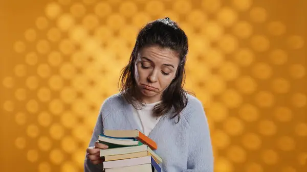 stock image Portrait of woman browsing through stack of textbooks, gathering information for school exam, isolated over studio background. Person searching necessary course for exam in pile of books, camera B