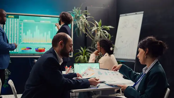 stock image Public relations team creating marketing campaigns and promotional activities in a boardroom, collaborating on new development plan. Employees reviewing sales trends metrics on pc. Camera B.