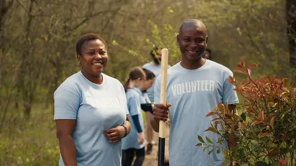 stock image Portrait of a couple volunteering to plant trees and collect trash from the woods, hold shovel and showing devotion for ecological justice. Environment activists fight nature conservation. Camera A.