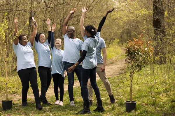 Stock image Diverse team of activists uniting hands in celebration after a successful mission of preserving nature, fighting for reforestation. Group of people joining forces to grow more trees in the woods.