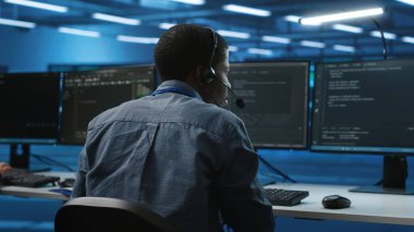 Bilgi işlem destek uzmanı kulaklıkla veri depolama ekipmanları hakkında konuşuyor. Çalışan, bilgisayar işlemleri yapan veri merkezi raflarını onarmak için uzmanla uzaktan sohbet ediyor