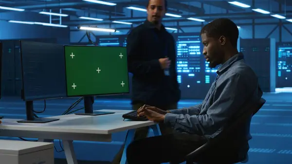 stock image Technician upgrading equipment in data center using isolated screen display. Professional at PC desk in high tech establishment overseeing server rows with chroma key monitor, panning shot