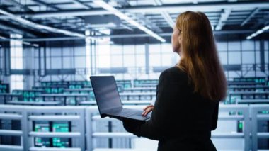 Sunucu çiftliğindeki sistem yöneticisi, yavaş veri aktarım oranlarına yol açan ağ sorunlarını düzeltmek için dizüstü bilgisayar kullanıyor. Veri merkezinde bilgi işlem personeli süper bilgisayarları etkileyen hataları düzeltiyor, kamera B