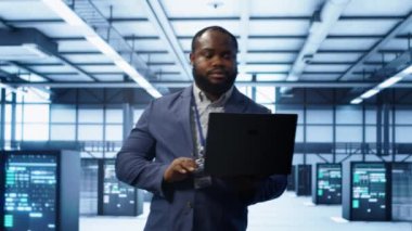 Modern veri merkezinde dizüstü bilgisayar üzerinde çalışan bilişim mühendisi, sunucu işlemleri, sistem bakımı ve siber güvenlik protokolleri, optimal performans ve veri bütünlüğü sağlanması, kamera A