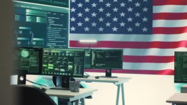 Siber istihbarat ve güvenlik operasyonları merkezi. Büyük ekranda ABD bayrağı var. Hükümetin siber güvenlik stratejisinin, dijital adli tıbbın ve siber tehditlere karşı korunmanın altını çiziyorum. Kamera A.