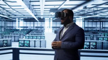 Afrikalı Amerikalı müteahhit veri merkezinde sanal gerçekliğe daldı, ünitelerin bakımını yapıyor. Sunucu performansını optimize etmek için VR kulaklık kullanan teknisyen, işlemleri kontrol ediyor, kamera A