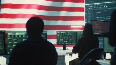 Amerikan bayrağı taşıyan bir hükümet teknoloji odasında siber savunma uzmanları. Siber güvenliği korumak ve korumak için güvenli bilgisayar, dijital adli tıp ve siber operasyonlar üzerinde çalışıyorum. Kamera A.