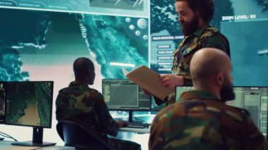 Ordu binbaşısı bir kontrol merkezindeki bir dava dosyasından operasyon detaylarını okur, lojistik veya operasyonel görevler için personel ve kaynakları yönetir. Görev gücü komutu. Kamera A.