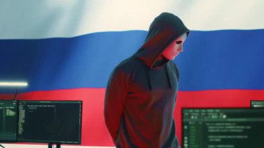 Rus bilgisayar korsanı, büyük ekranda Rus bayrağı ile birlikte, siber terör, fidye virüsü ve casuslukla uğraşıyor. Yanlış bilgilendirme ve saldırı propagandası yapmak. Kamera A.