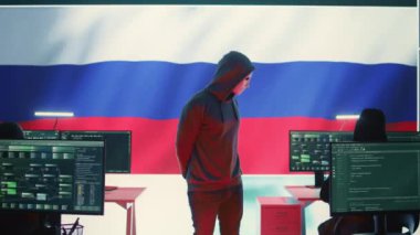 Rus bilgisayar korsanı, büyük ekranda Rus bayrağı ile birlikte, siber terör, fidye virüsü ve casuslukla uğraşıyor. Yanlış bilgilendirme ve saldırı propagandası yapmak. Kamera B.