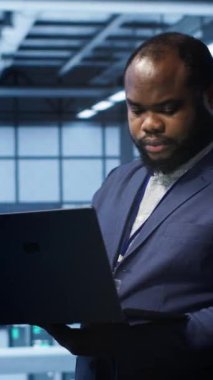 Dikey video Afrikalı Amerikan bilişim operatörü veri merkezi ekipman ömrünü uzatmak için dizüstü bilgisayar kullanıyor. Sunucu merkezi çalışma alanı izleme sunucu ana sistemlerinde bilişim uzmanı