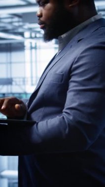 Sunucu merkezindeki dikey video yazılım geliştiricisi dizüstü bilgisayardaki kurtarma planını kontrol ediyor, donanım enerji tüketimini izliyor. Afrikalı Amerikalı işçiler veri merkezinde dizüstü bilgisayar kullanıyorlar.