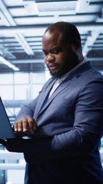 Dikey video Afrikalı Amerikan bilişim operatörü veri merkezi ekipman ömrünü uzatmak için dizüstü bilgisayar kullanıyor. Sunucu merkezi çalışma alanı izleme sunucu ana sistemlerinde bilişim uzmanı