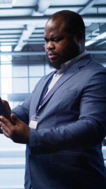 Sunucu merkezindeki dikey video geliştirici tablet üzerindeki kurtarma planını kontrol ediyor, donanım enerji tüketimini izliyor. Afrikalı Amerikalı işçiler veri merkezinde dijital cihaz kullanıyor.