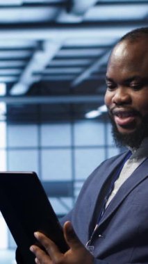 Aktarım oranlarını etkileyen ağ sorunlarını düzeltmek için tablet kullanarak sunucu odasındaki dikey video programcısı. Veri merkezindeki Afrikalı Amerikalı adam ana bilgisayarları etkileyen hataları düzeltiyor, kamera A