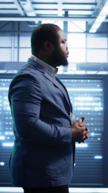 Veri merkezinde yürüyen dikey video Afrikalı Amerikalı teknisyen hataları tespit etmek için sistemleri izliyor. Sunucu merkezindeki adam teşhis koyuyor. İhtiyacı olan altyapı hatalarını arıyor.