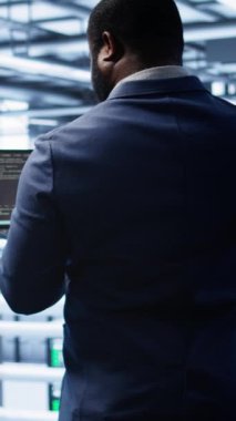 Veri merkezinde donanım hatalarını düzeltmek için tablet üzerinde hata kontrolü yapan dikey video Afrikalı Amerikalı yönetici. Sunucu merkezi çalışma alanı bilişim uzmanı ana bilgisayarları etkileyen sorunlar arıyor