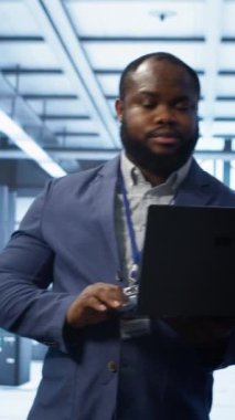 Modern veri merkezinde dizüstü bilgisayar üzerinde çalışan dikey video mühendisi, sunucu işlemleri, sistem bakımı ve siber güvenlik protokollerini denetleyerek, optimal performans ve veri bütünlüğünü güvence altına alıyor