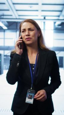 Veri merkezinde akıllı telefondan konuşan dikey video yazılım mühendisi sunucu bakım görevlerini koordine ediyor. Sunucu rafları ve yüksek teknoloji ekipmanlarıyla çevrili bir kadın, telefon görüşmesi sırasında konuşuyor.