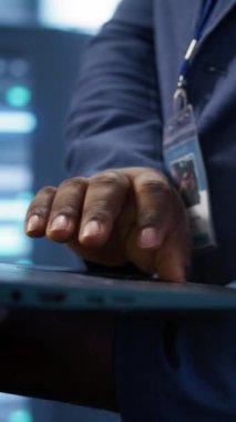 Veri merkezinde dizüstü bilgisayar üzerinde çalışan dikey video teknisyeni sunucu işlemlerini denetliyor. Sunucu merkezinde optimum performans ve veri bütünlüğünü sağlayan adamın aşırı yakın plan çekimi, kamera B