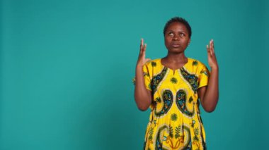 Muhteşem bir kadın kendini pozitif hissediyor ve stüdyoda dua ediyor. Mavi arka plana karşı ruhaniyete olan inancını ve umudunu gösteriyor. Genç yetişkin iyimser, çiçekli kabile kıyafetleri. Kamera B.