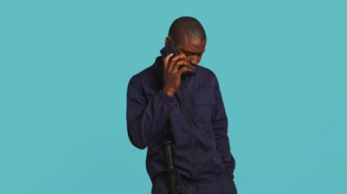 İşyerindeki güvenlik görevlisinin portresi mekanı denetlerken arkadaşlarını aramak için telefon kullanıyor. Özel güvenlik görevlisi arkadaşlarıyla telefon görüşmesi yapıyor, stüdyo arkaplanı, kamera B