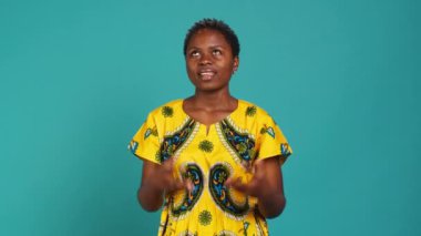 İyimser, büyüleyici kız biraz şans ve servet için dua ediyor. Mavi arka planda olumlu ve umut dolu hissediyor. Stüdyoda geleneksel kabile kıyafeti giyen genç bir kadın. Kamera A.