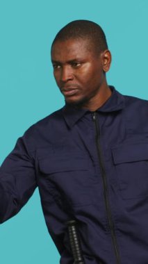 Güvenlik görevlisinin dikey video portresi insanları işaret ediyor, onları uyarıyor ve atölyenin arka planında görev alıyor. Afrikalı Amerikalı muhafız izinsiz girenleri azarlıyor, güvenliği sağlıyor.